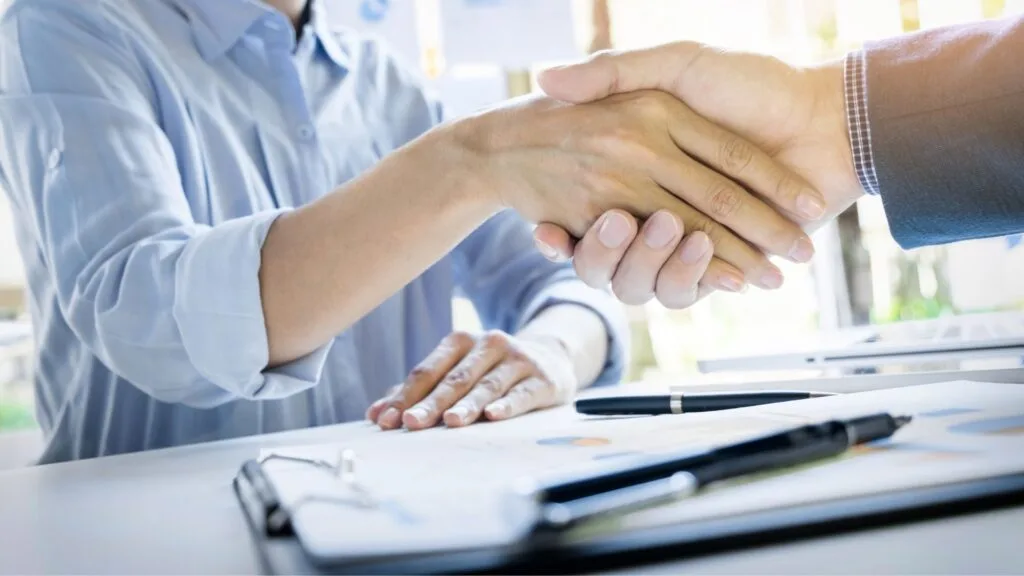 Two professionals shake hands over a contract, highlighting clear payment terms in manufacturing to prevent delays and improve cash flow.